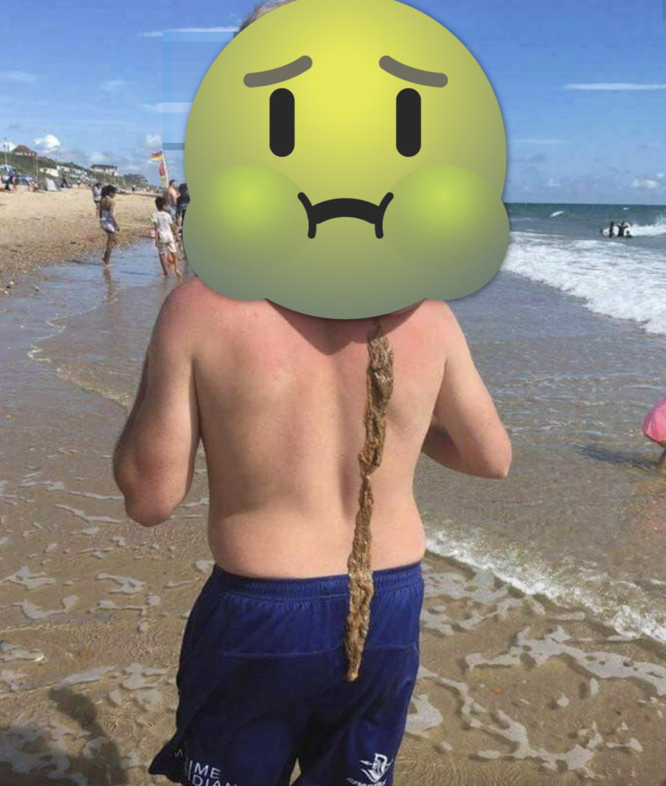 A shirtless man carries a child on his back at a beach; the child's poo runs down the man's back, and his head is covered by a huge "sick" emoji