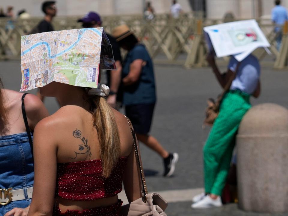 Tourists shelter beneath maps as they wait for the start of Pope Francis' Angelus noon prayer in St. Peter's Square in Vatican City on July 9, 2023.