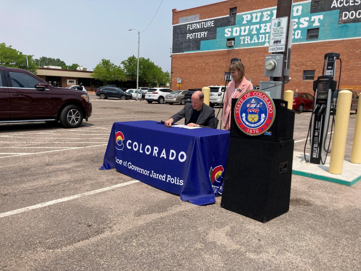 Colorado Gov. Jared Polis is joined by state Rep. Tisha Mauro as he signs a law expanding regulations for electric vehicles next to an EV charging station in Pueblo on May 23, 2023. Mauro was one of the prime sponsors of the legislation.