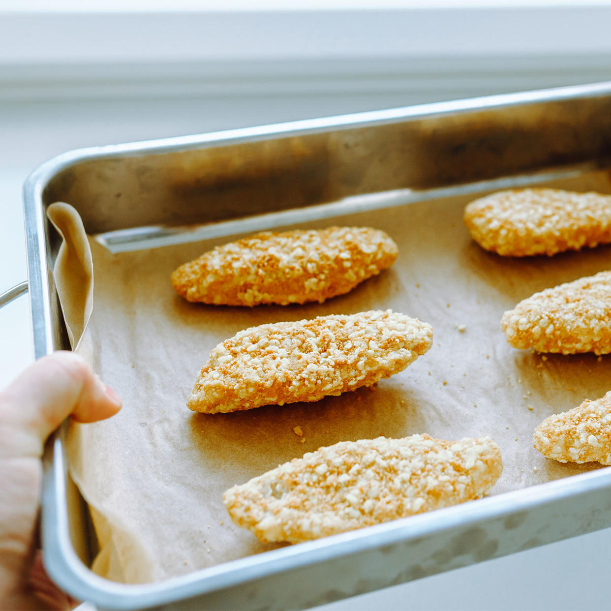 person holding a pan of frozen breaded chicken tenders