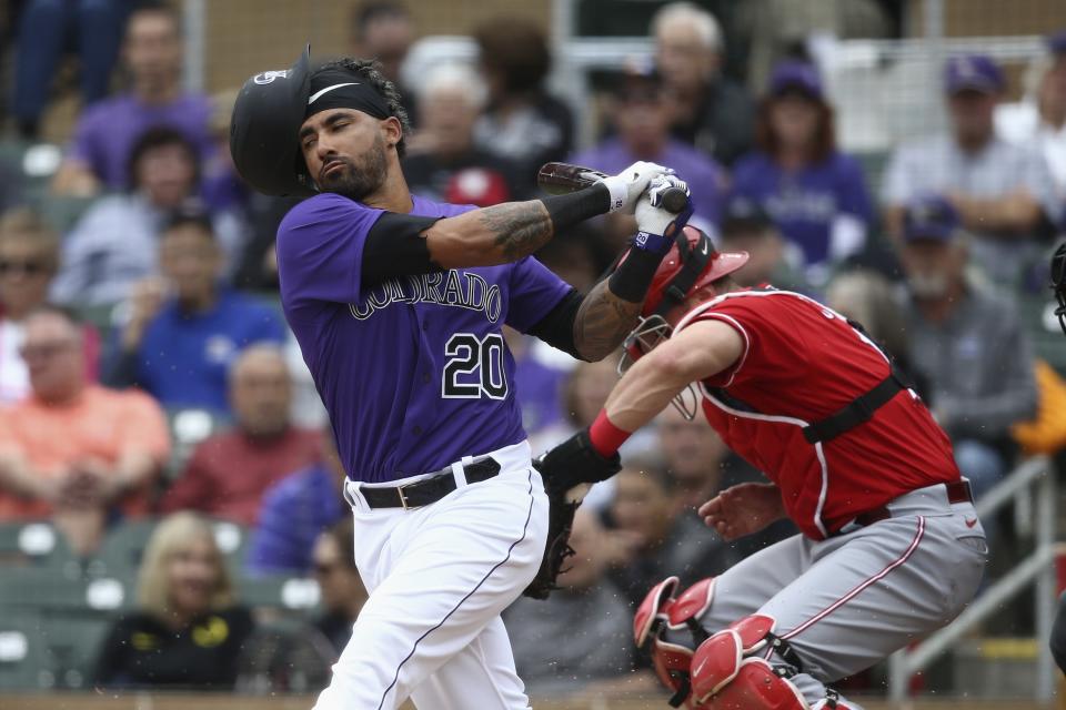 Colorado Rockies' Ian Desmond (20) loses his helmet on a swing as Cincinnati Reds catcher Curt Casali, right, gets out of the way during the second inning of a spring training baseball game Tuesday, March 10, 2020, in Scottsdale, Ariz. (AP Photo/Ross D. Franklin)