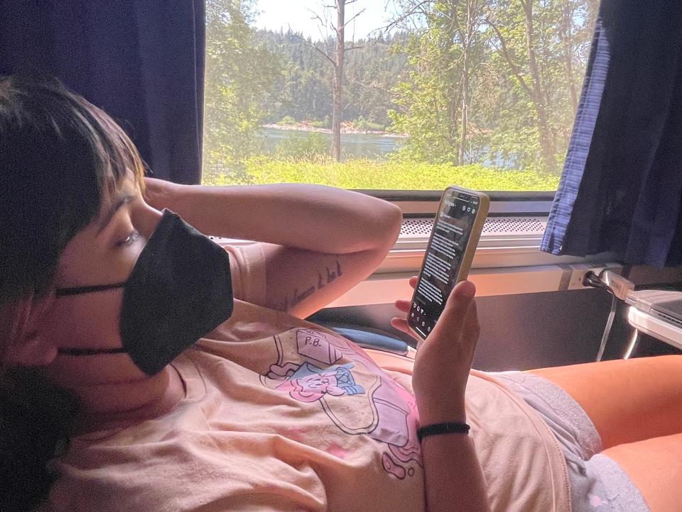 the writer's wife wearing a mask, on her phone, on the train