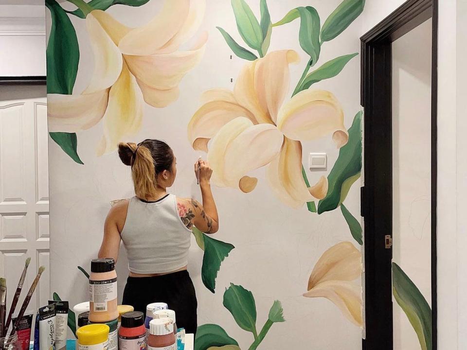 A progress image of Toh painting lilies and irises onto a kitchen wall. The painting extends past the door frame and into the next room.