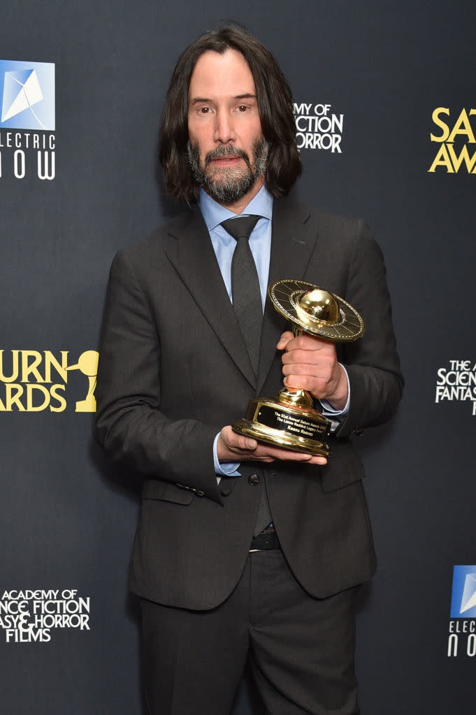 Keanu Reeves in a classic suit holding a Saturn Award trophy