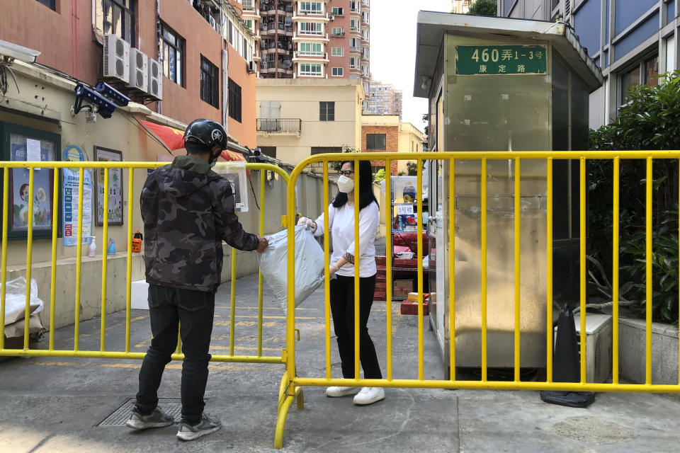 A woman wearing a face mask reaches through a barricade to receive a delivery package in Shanghai, China, Saturday, May 21, 2022. (AP Photo/Chen Si)