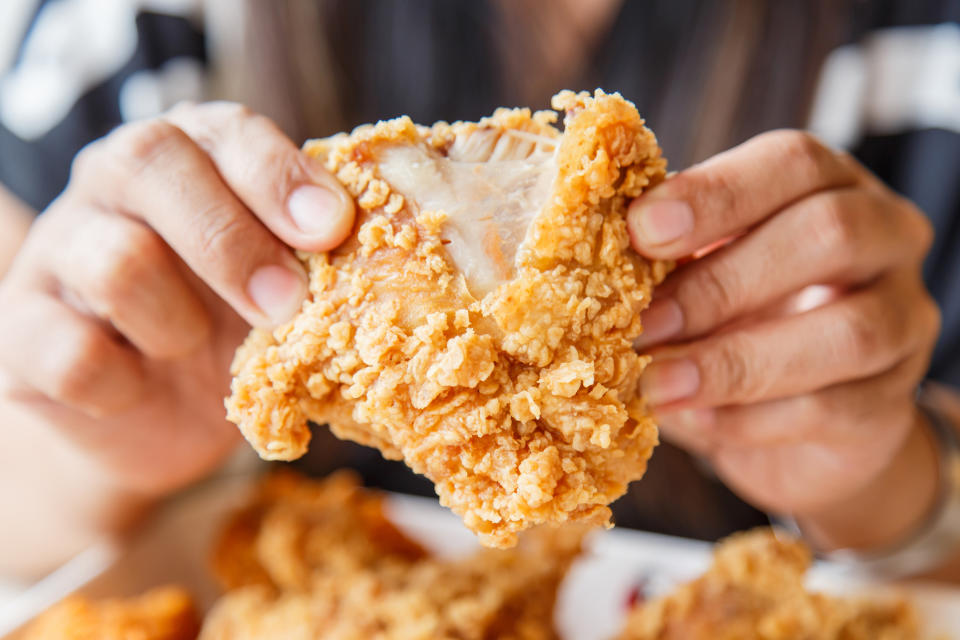 A close-up of a person's two hands breaking a part a piece of fried chicken