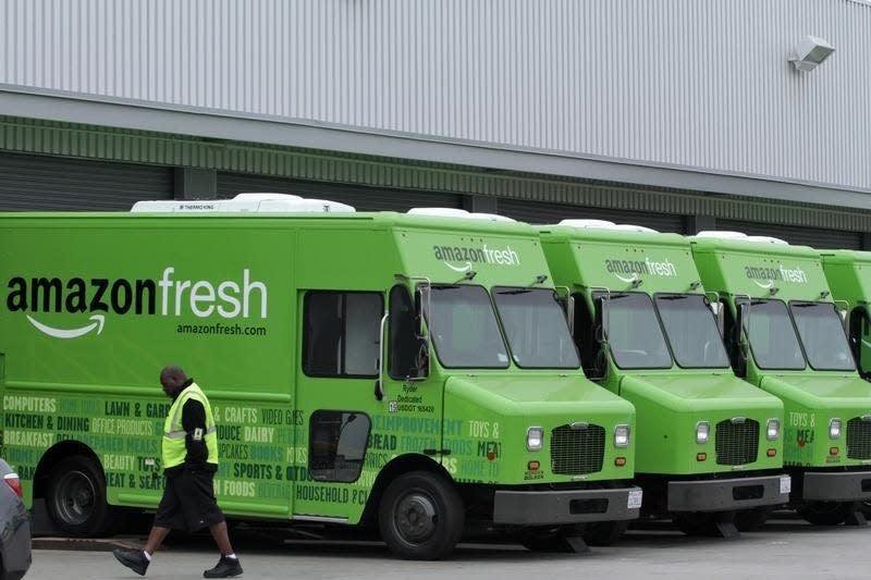 A worker walks past Amazon Fresh delivery vans parked at an Amazon Fresh warehouse in Inglewood, California, June 14, 2013.  REUTERS/Jonathan Alcorn 