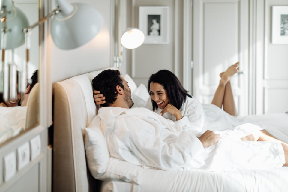 Couple laughing together under sheets in a bed, appearing intimate and happy