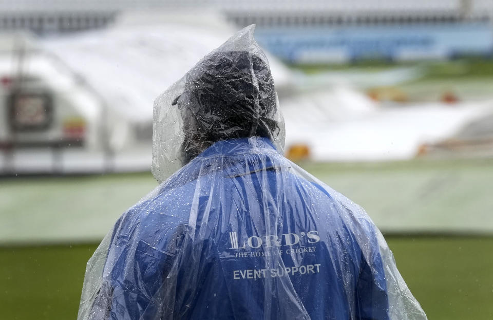 A steward wears a rain cape as he waits, as rain delays the start of play on the third day of the Test match between England and New Zealand at Lord's cricket ground in London, Friday, June 4, 2021. (AP Photo/Kirsty Wigglesworth)