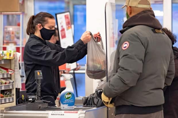 A cashier wearing a mask to help slow the spread of COVID-19. Nunavut announced Sunday that masks are now mandatory territory wide. (Natalie Maerzluft/Reuters - image credit)