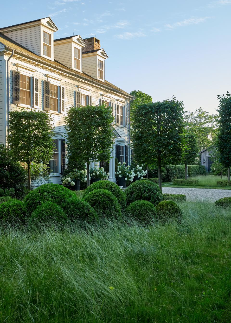 Pleached linden trees and boxwoods frame the whitewashed façade of the colonial-style main house.