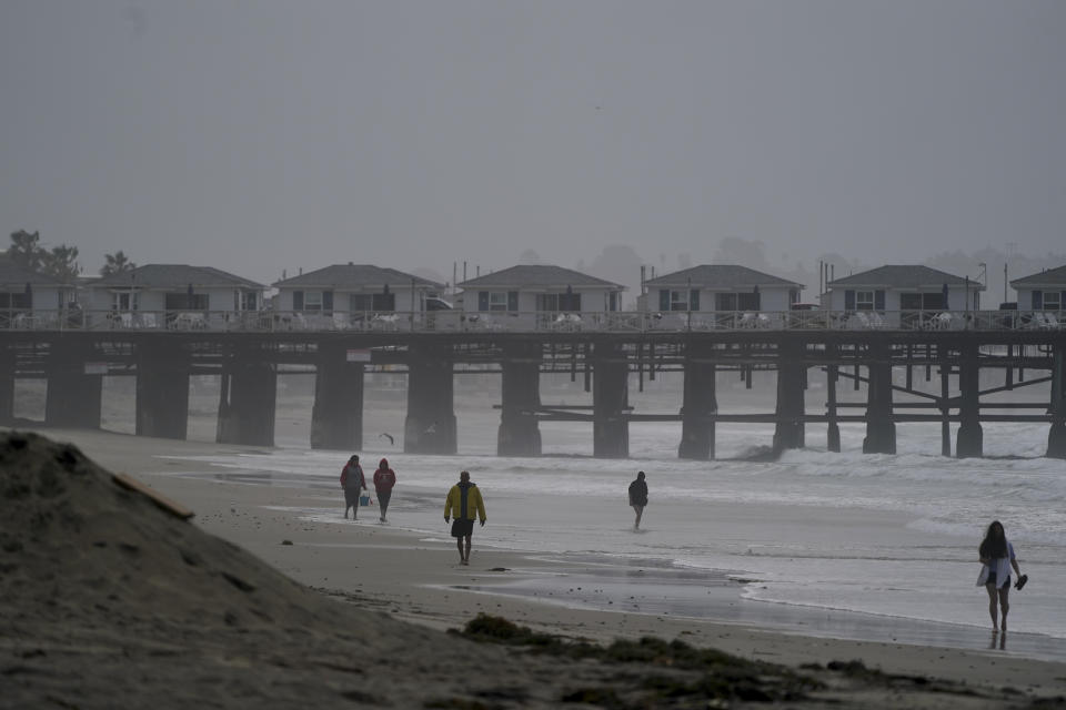 People walk along a beach after hours of intense rain, Tuesday, March 21, 2023, in San Diego. Californians are tired. Tired of the rain, tired of the snow, tired of stormy weather and the cold, relentlessly gray skies that have clouded the Golden State nearly nonstop since late December. (AP Photo/Gregory Bull)