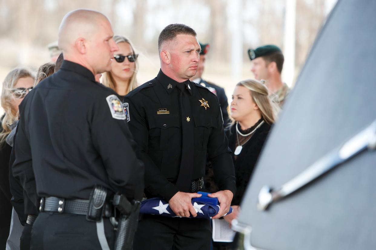 DeSoto County Sheriff's Department deputy Nicholas Cook holds a folded flag while looking into the hearse where K9 officer Luca was placed after a service was held for him at Longview Point Baptist Church in Hernando, Miss., on Wednesday, February 28, 2024. Luca was shot after a suspect fleeing in a car was brought to a stop by deputies. After the stop, K9 Luca was released and the person shot the dog.