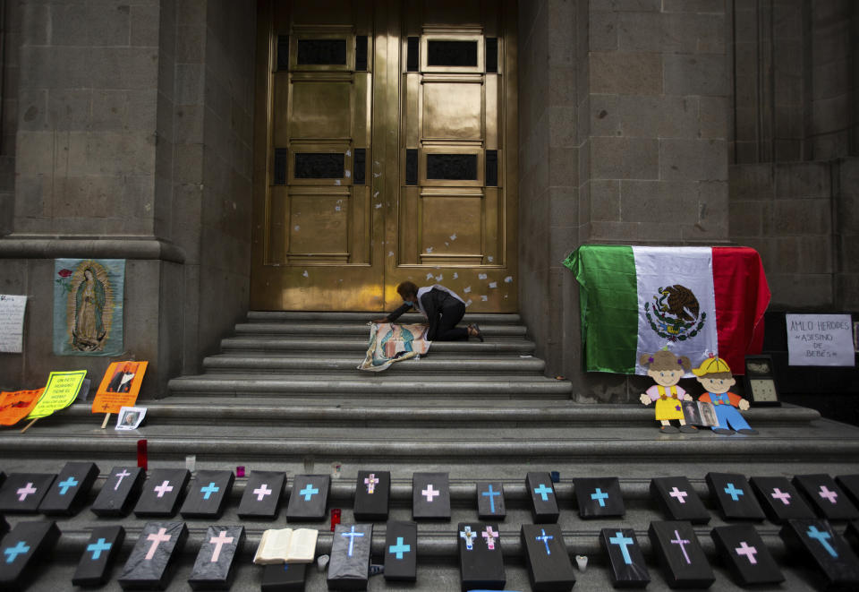 An activist against abortion places an image of Our Lady of Guadalupe alongside small, mock coffins at the entrance to the Supreme Court to celebrate the court's decision against an injunction in Veracruz state that aimed to decriminalize abortion for all cases within the first 12 weeks of pregnancy, in Mexico City, Wednesday, July 29, 2020. Two of Mexico’s 32 states have decriminalized abortion. (AP Photo/Fernando Llano)