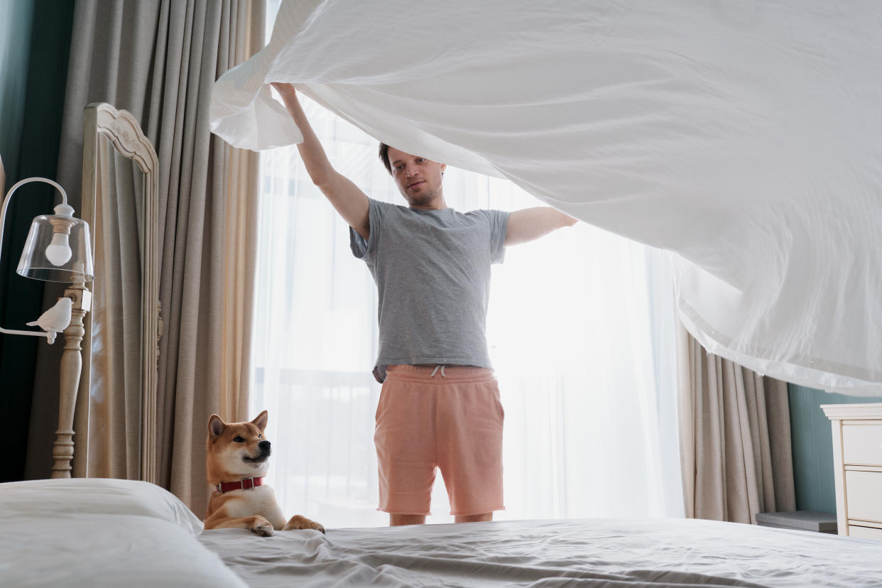 Young man putting the bedding cover on the bed. (Photo: Getty)