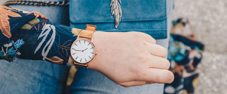 street style fashion details. close up, young fashion blogger wearing a floral jacker, and a white and golden analog wrist watch. checking the time, holding a beautiful suede leather purse.