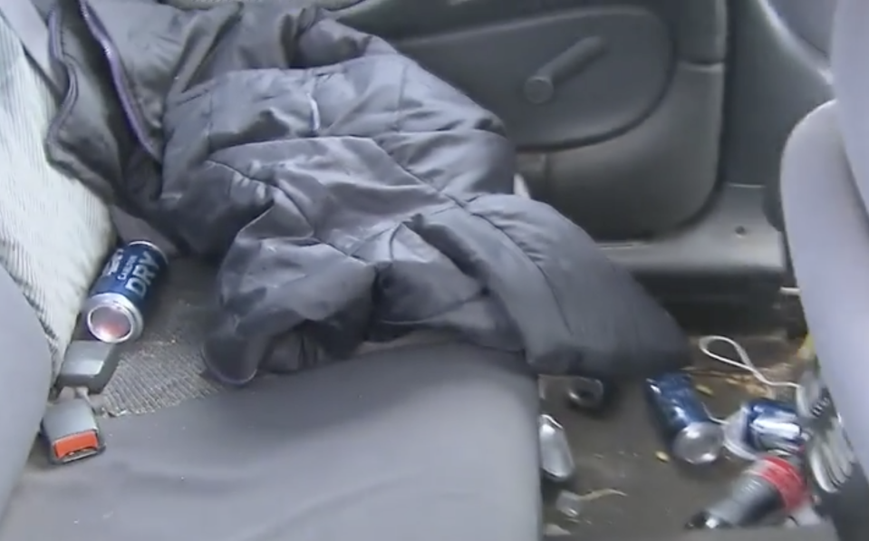 The inside of the car with bottles and cans throughout the back seat.