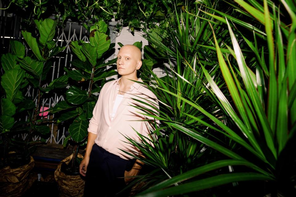 A man poses in front of a shop selling plants.