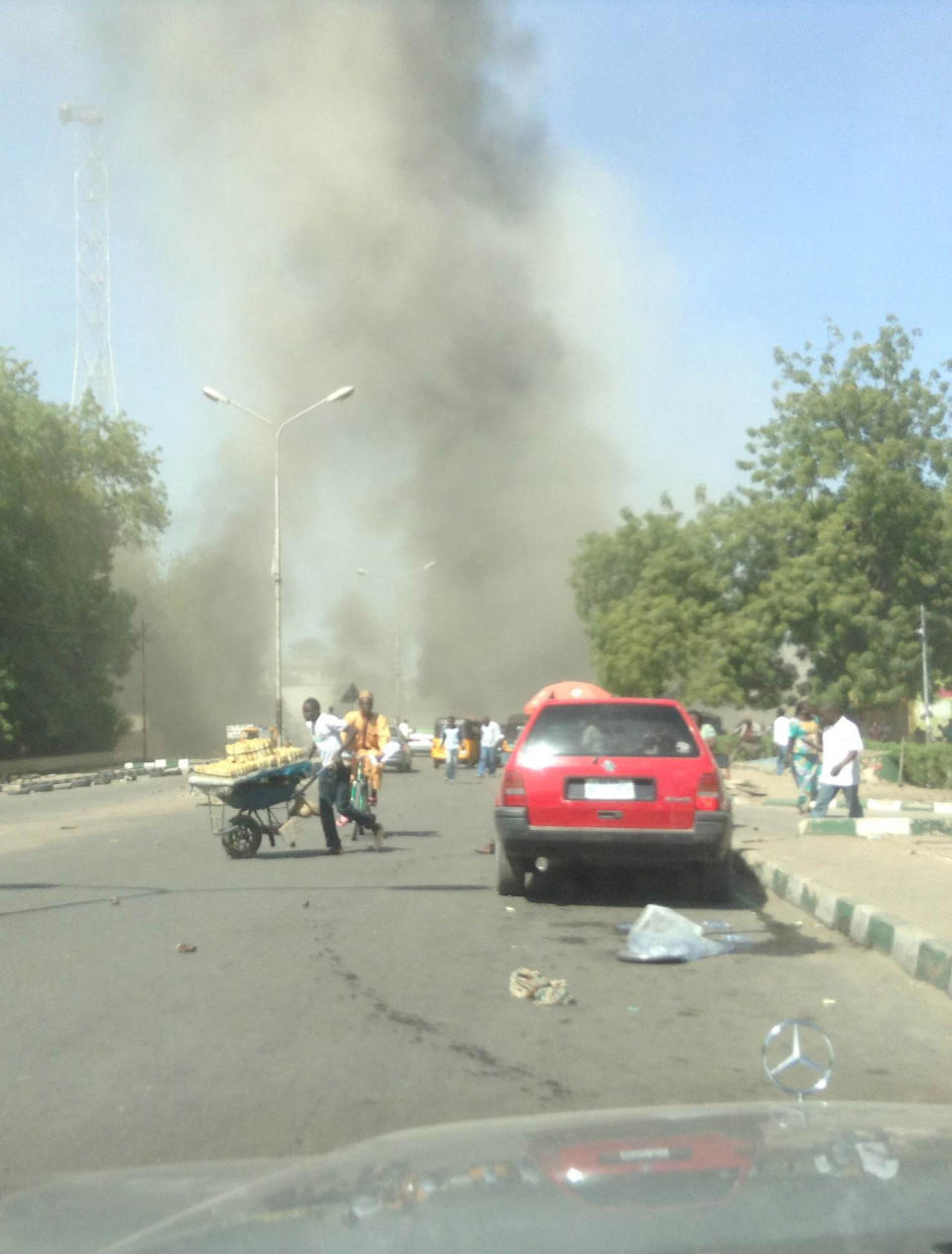 In this photo taken with a mobile phone, people runs as smokes billows through the sky after a car bomb explosion at a military post in Maiduguri, Nigeria, Tuesday, Jan. 14, 2014. A vehicle exploded at a military post in a commercial area in a northeastern Nigerian city on Tuesday, killing at least 17 people and causing pandemonium with blood-spattered bystanders running away and vehicles colliding as drivers rushed to flee. (AP Photo/Abdulkareem Haruna)