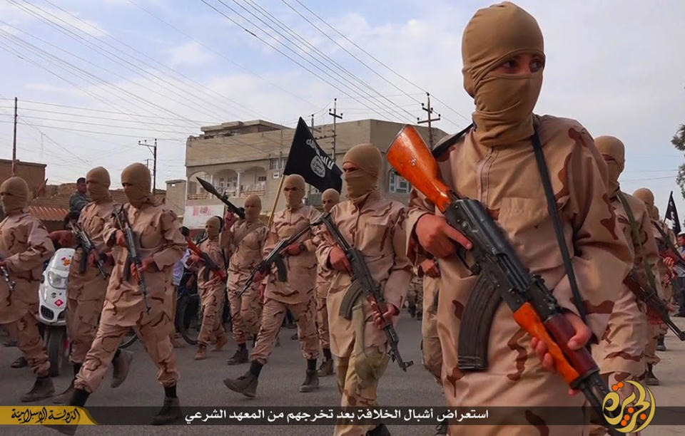 FILE - In this file photo released on April 25, 2015, by a militant website, which has been verified and is consistent with other AP reporting, young boys known as the "caliphate cubs" hold their rifles as they parade after graduating from a religious school, in Tal Afar, near Mosul city, north Iraq. The Arabic words, center, read: "A parade of caliphate cubs after their graduation from a religious school." (Militant website via AP, File)