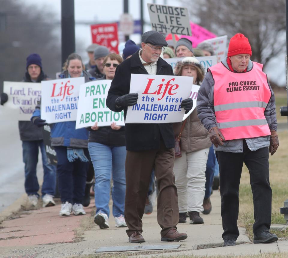 A Northeast Ohio Women's Center clinic escort, right, walks alongside anti-abortion marchers Saturday on State Road in Cuyahoga Falls. The clinic provides escorts for women entering the clinic who may be confronted by protesters.