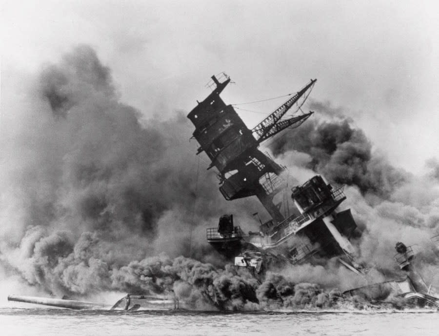 FILE – The battleship USS Arizona belches smoke as it topples over during a Japanese surprise attack on Pearl Harbor, Hawaii, on Dec. 7, 1941. The Navy and the National Park Service will host a remembrance ceremony Thursday, Dec. 7, 2023, marking the 82nd anniversary of the attack on Pearl Harbor that launched the U.S. into World War II. (AP Photo/File)