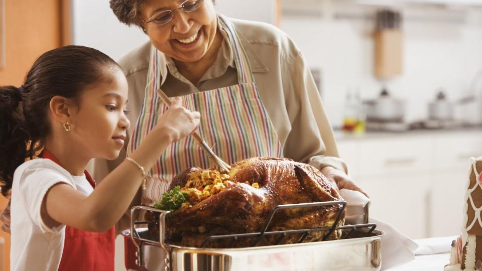 hispanic granddaughter helping grandmother baste turkey