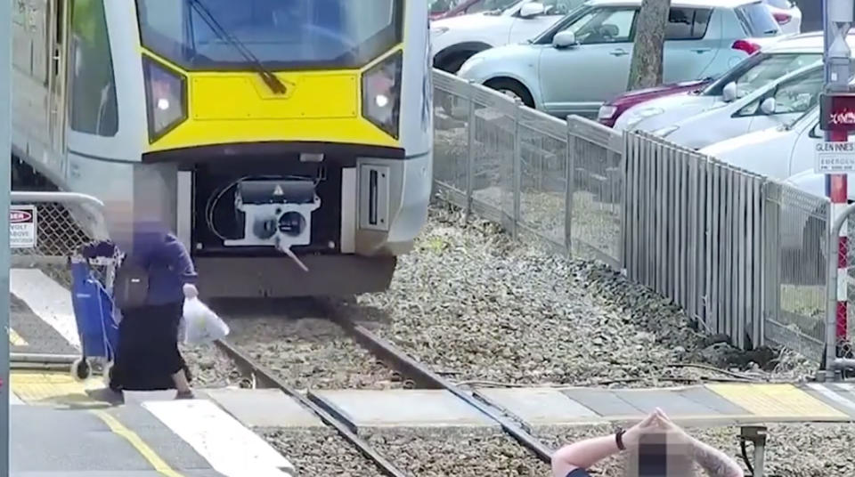 An elderly woman with a trolley crosses in the path on an incoming train in New Zealand.