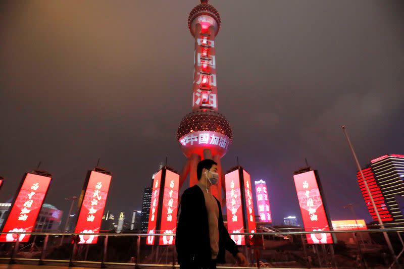 Man wearing a face mask walks past the Oriental Pearl Tower lit with messages reading "Stay strong China", on the Lantern Festival in Shanghai