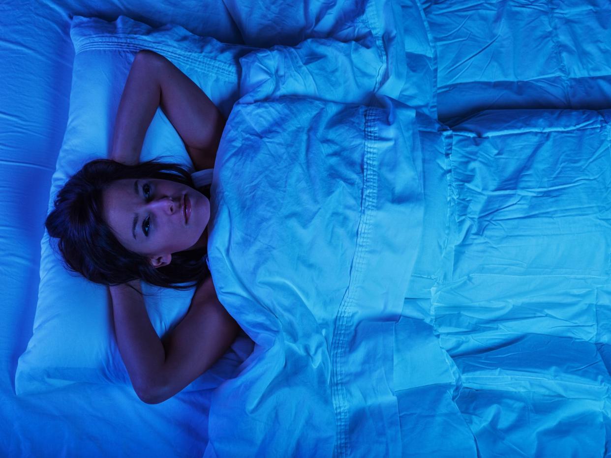 Photo of a young woman lying in bed at night, wide awake with a case of insomnia