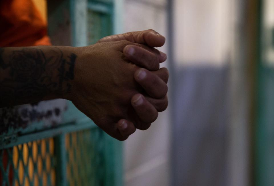 A female inmate leans against her cell door.