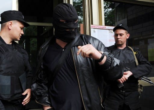 A man wearing a balaclava walks past two policemen holding submachine guns as they guard an entrance to the house of Alexei Navalny, an opposition leader and a popular anti-corruption blogger, in Moscow on June 11, 2012. Police armed with assault rifles raided the homes of Russia's top protest leaders on June 11 in a show of force on the eve of a mass Moscow rally against President Vladimir Putin