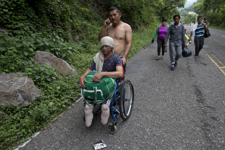 In this Oct. 16, 2018 photo, Honduran migrant Omar Orella pushes fellow migrant Nery Maldonado Tejeda in a wheelchair, as they travel with hundreds of other Honduran migrants making their way the U.S., near Chiquimula, Guatemala. Maldonado said he lost his legs in 2015 while riding "The Beast," a northern-bound cargo train in Mexico, and that this is his second attempt to reach the U.S. (AP Photo/Moises Castillo)