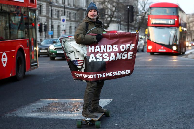 FILE PHOTO: A man rides a skateboard holding a banner with an image of Julian Assange in London