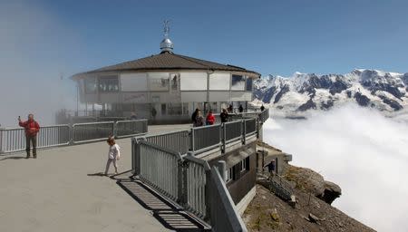 Tourists are seen in front of the world's first revolving restaurant, known as Piz Gloria from the 1969 James Bond movie "On Her Majesty's Secret Service", which was filmed there, on the peak of the Schilthorn mountain (altitude 2970 m/ 9744 feet) at the Bernese Oberland, Switzerland August 7, 2012. REUTERS/Arnd Wiegmann/Files