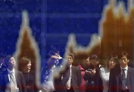 Passerbys are reflected on a graph showing recent Japan's Nikkei share average movements outside a brokerage in Tokyo March 30, 2015. REUTERS/Issei Kato