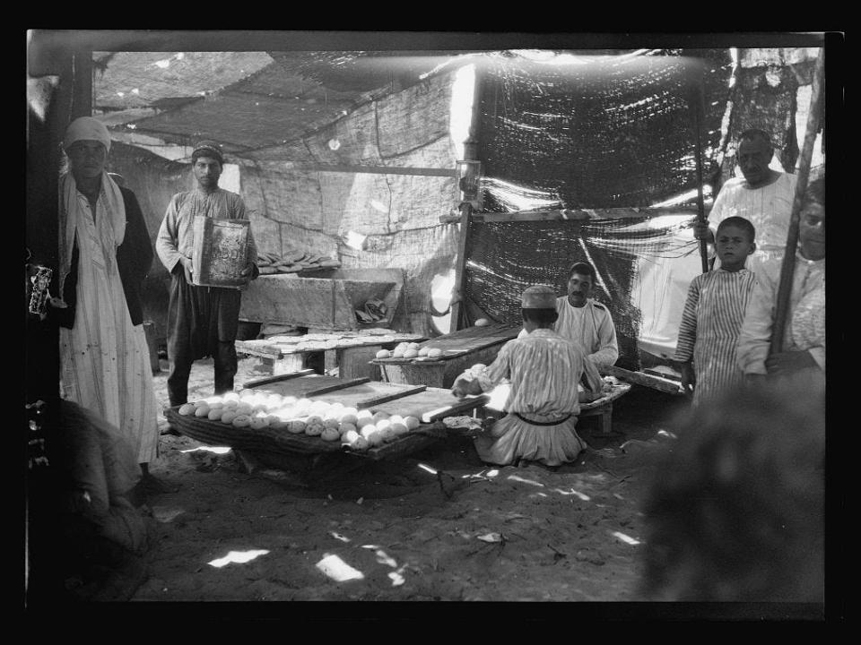 A black and white photo of people inside a mat shanty making bread.