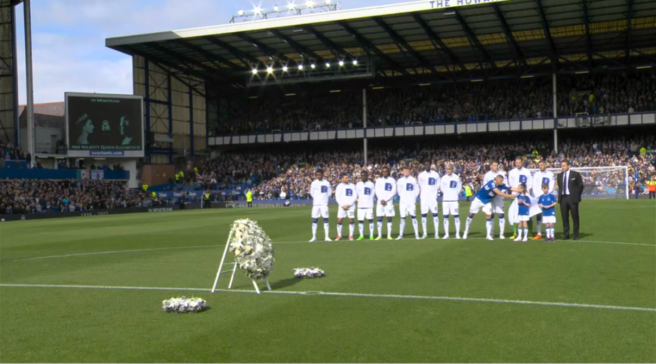 Everton's Vitalii Mykolenko, centre right, gives his jacket to a mascot struggling with the cold during the minute's silence at Goodison Park
