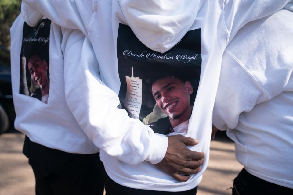 The back of white sweatshirts worn by mourners depict a smiling young man next to a candle