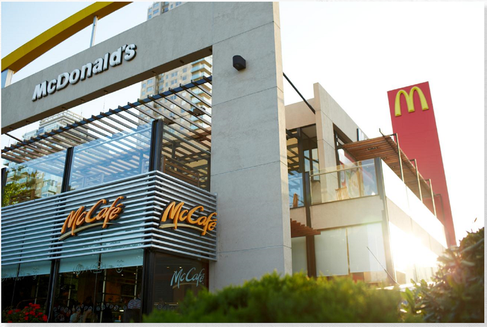 McDonald's store on two stories with shrubbery nearby and sun shining.