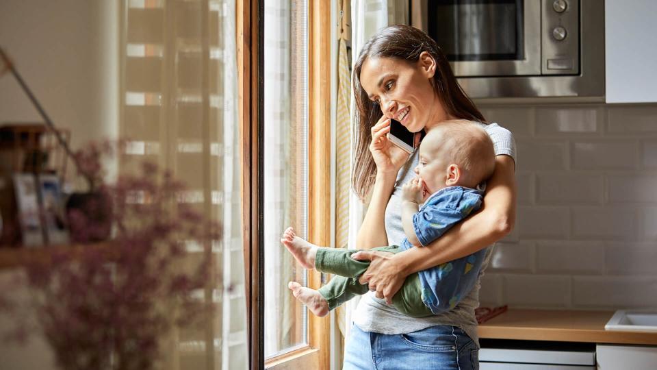 Smiling woman talking on mobile phone while carrying baby.