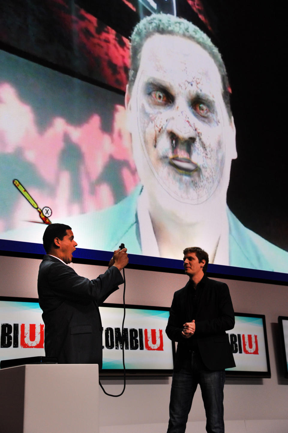 FILE - In this June 5, 2012 publicity file photo provided by Nintendo of America, Reggie Fils-Aime, Nintendo of America's President and Chief Operating Officer, left, tests out an interactive feature of "ZombiU," an upcoming Ubisoft game for the Wii U console, during the Nintendo All-Access Presentation at E3 2012 in Los Angeles. Using facial recognition, the feature transforms the player into a gruesome zombie. (AP Photo/Nintendo of America, Vince Bucci, File)