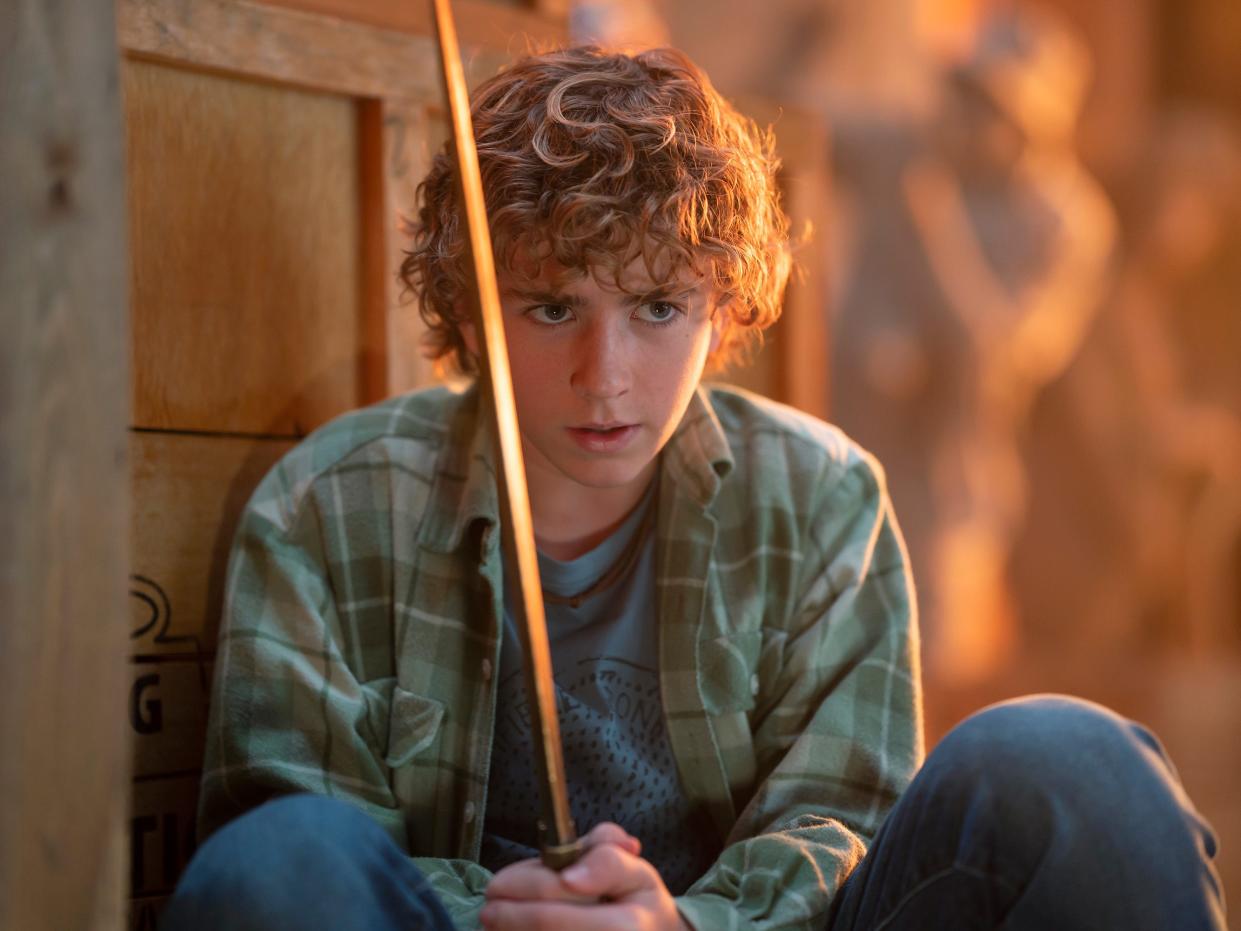percy jackson in the disney plus live action show, crouching behind a crate and intently holding a gleaming golden sword