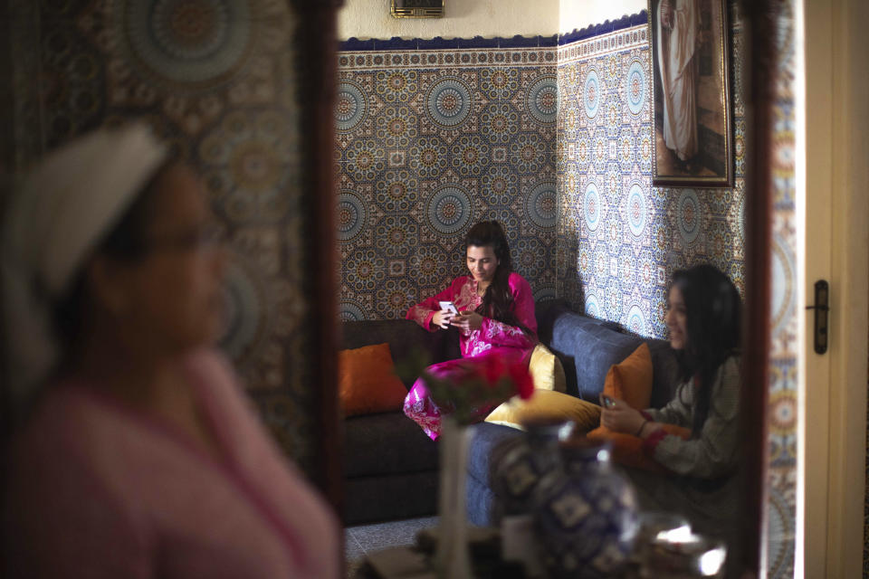 Family members Zineb Jammar, center, and Fadila Lahta, right, use their electronic devices as they spend the first day of Eid in lockdown due to the Coronavirus pandemic, in Sale, Morocco, Sunday, May 24, 2020. (AP Photo/Mosa'ab Elshamy)