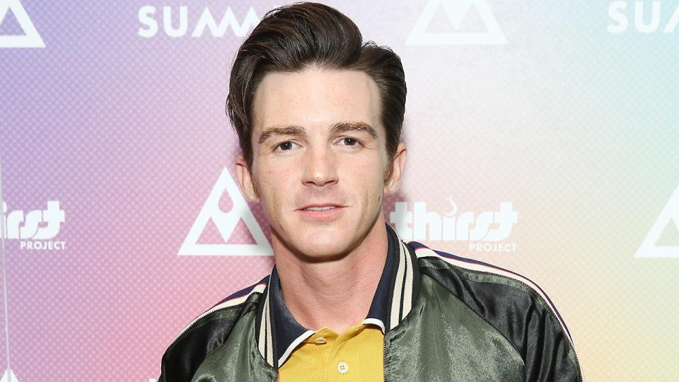 Drake Bell wears a green jacket and yellow under shirt with a blue striped collar on the red carpet