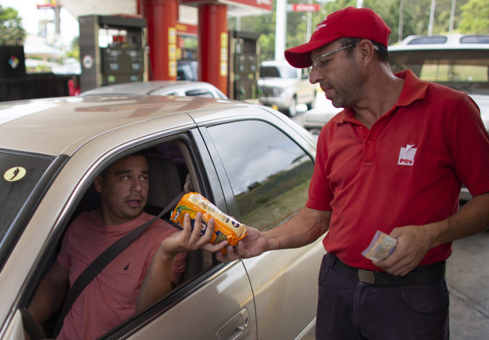 In this Oct. 8, 2019 photo, gas station attendant Orlando Godoy takes a package of corn flour as payment after filling a motorist's tank, which costs a tiny fraction of a U.S. penny, in San Antonio de los Altos on the outskirts of Caracas, Venezuela. The economy is in such shambles that drivers are now paying for fill-ups with a little food, a candy bar or just a cigarette. (AP Photo/Ariana Cubillos)