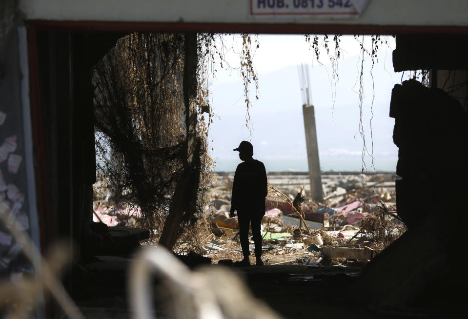 In this Friday, Oct. 5, 2018, file photo, a man is silhouetted as he scavenges for usable items at a tsunami-ravaged area in Palu, Central Sulawesi, Indonesia. (AP Photo/Dita Alangkara, File)