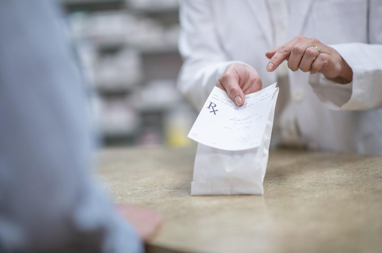 A pharmacist handing a customer a  packaged prescription.