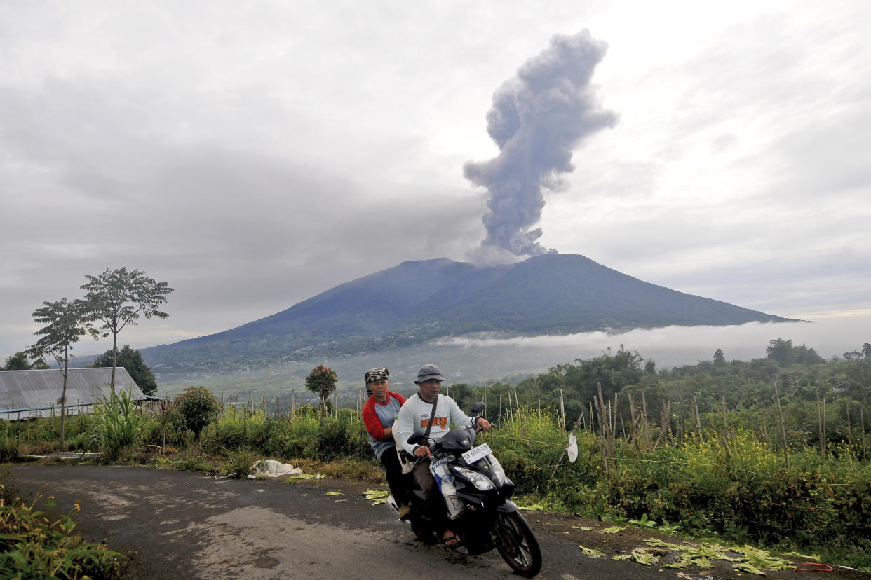 Two people on a motorbike ride along he coast as Mount Marapi in the distance spews volcanic ash.