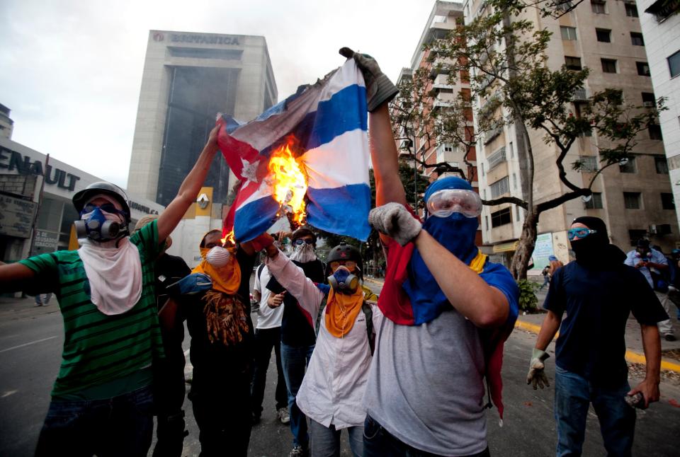 Demonstrators burn a Cuban flag during clashes at an anti-government protest in Caracas, Venezuela, Friday, March 7, 2014. Venezuela is coming under increasing international scrutiny amid violence that most recently killed a National Guardsman and a civilian. United Nations human rights experts demanded answers Thursday from Venezuela's government about the use of violence and imprisonment in a crackdown on widespread demonstrations. (AP Photo/Alejandro Cegarra)